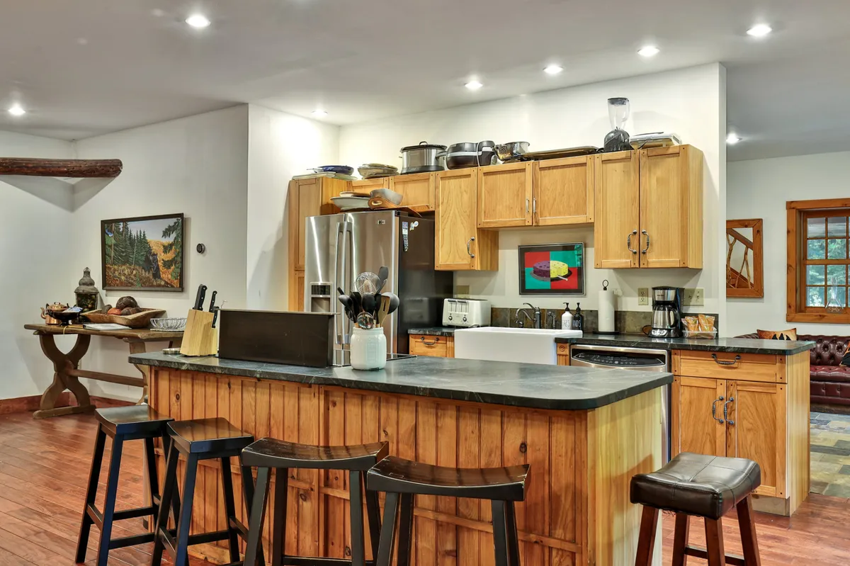 A spacious kitchen with a central island, wooden cabinetry, stainless steel appliances, framed artwork, and a decorative table. The space is designed for casual dining, entertaining, and enjoying group meals.