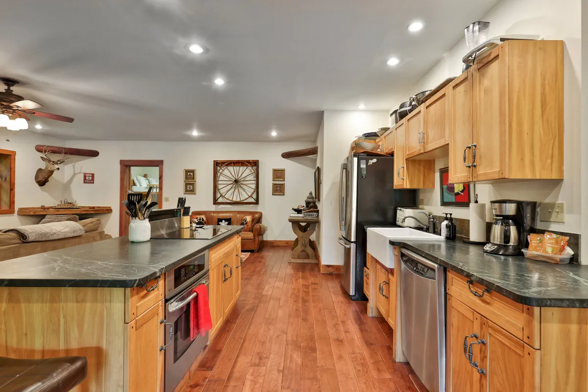 A welcoming kitchen space with a large island, wood cabinetry, stainless steel appliances, and a view into the living area beyond. The open flow encourages cooking, entertaining, and gathering, enhanced by warm lighting and comfortable finishes.