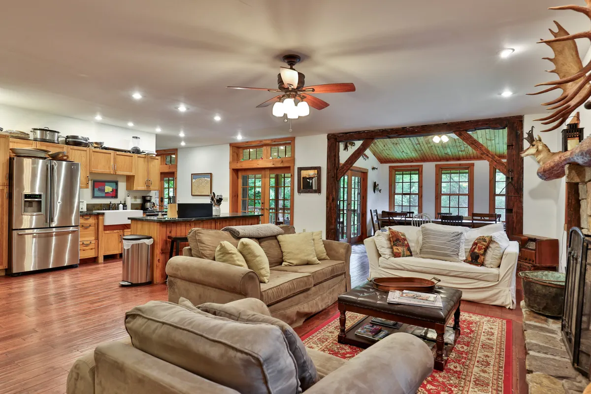 The hero image showcases a spacious, open-concept living area with plush, comfortable sofas gathered around a cozy fireplace. Exposed wooden beams add rustic charm, while the adjacent kitchen area is perfect for entertaining or casual family meals. The warm lighting and inviting layout create an atmosphere ideal for relaxing, celebrating, and connecting with loved ones.