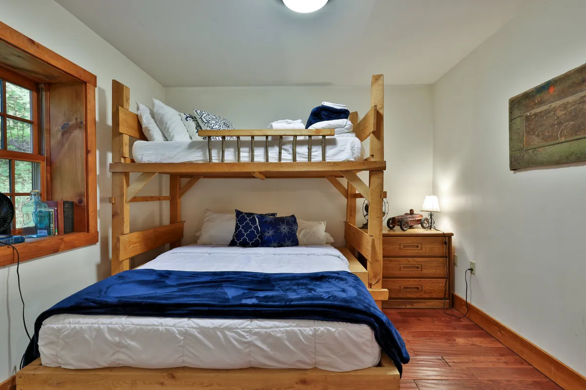 A playful bedroom with bunk beds dressed in blue bedding, wooden furniture, and a window that lets in natural light, creating a cozy and fun environment ideal for younger guests.
