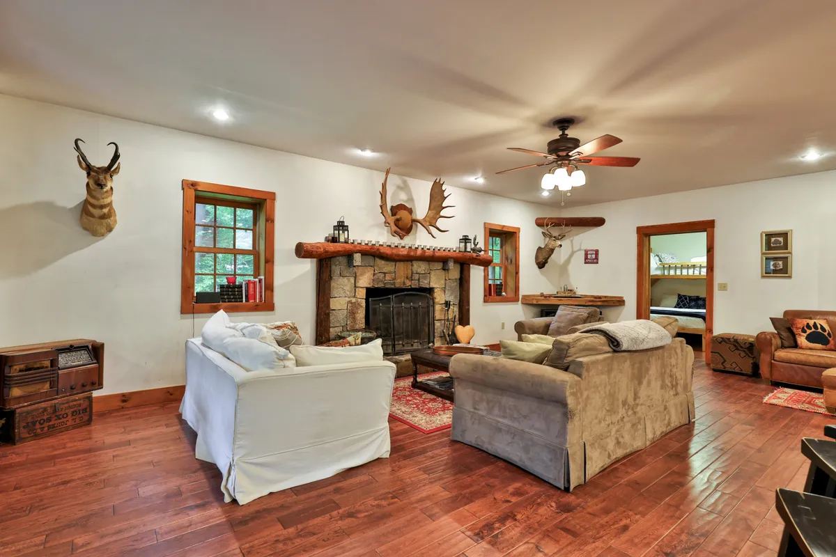 A warm living area centered around a fireplace, with a comfortable sofa, wooden beams, and subtle mountain lodge decor. The scene suggests relaxation, intimate gatherings, and cozy evenings by the fire.