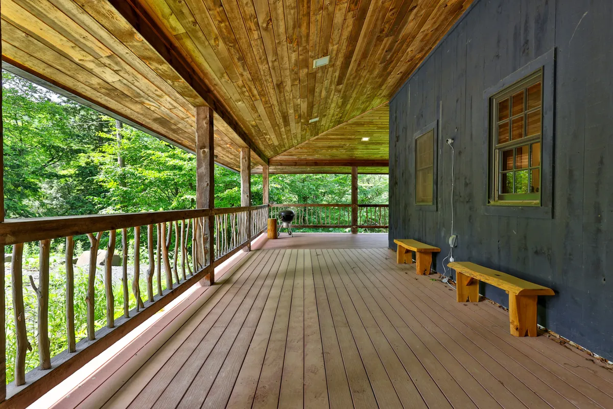 This image captures the lodge's expansive exterior wraparound porch with wooden railings, surrounded by natural scenery. Benches and cozy outdoor seating invite groups to gather, relax, and enjoy the views. The scene hints at both daytime and evening uses, such as morning coffee rituals or sunset barbecues.