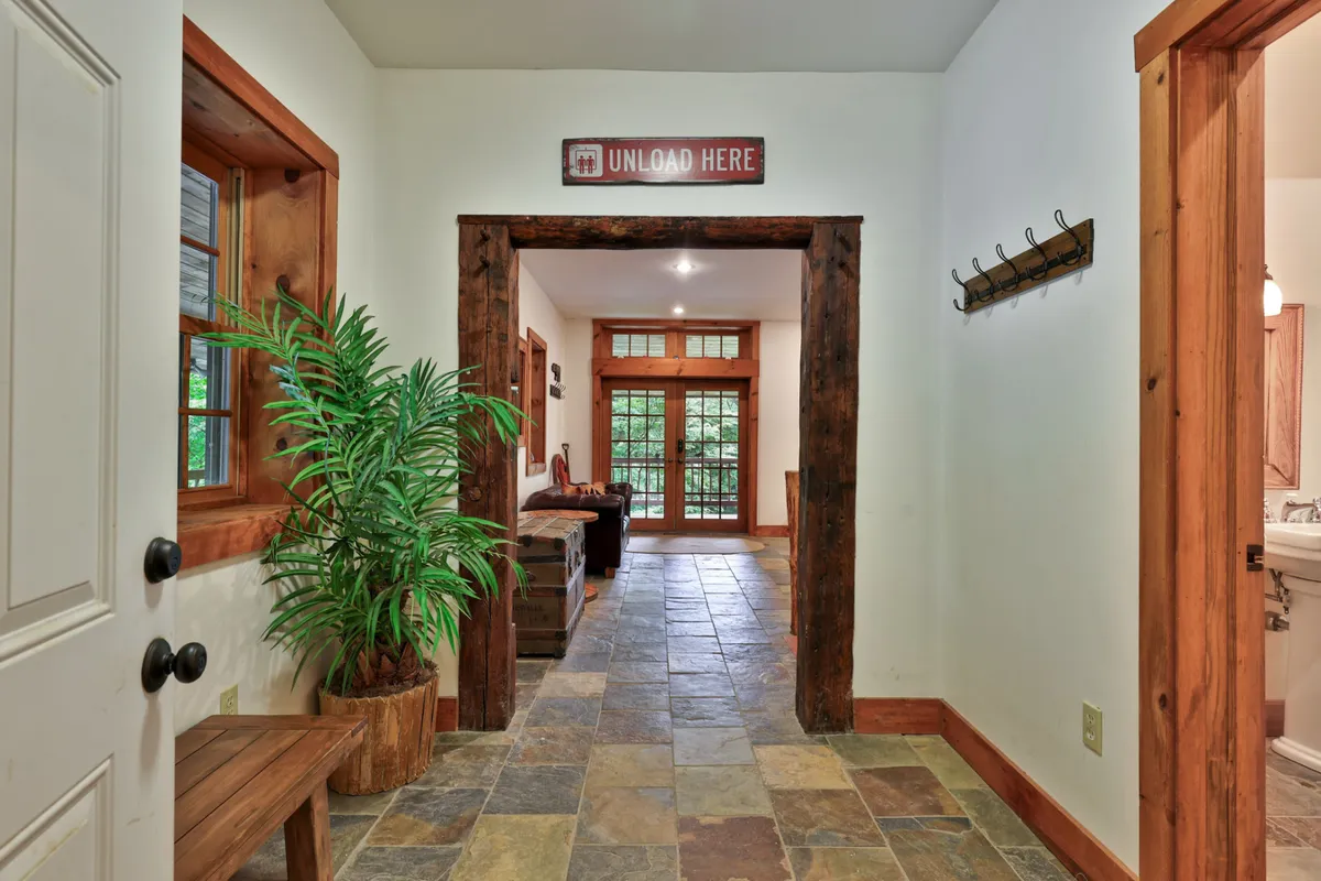 The welcoming front entryway features a rustic wooden door, potted plant, wooden bench, and arched doorway, setting a warm and hospitable tone. The slate flooring and entry space suggest a seamless transition from the outdoors into the home—a gathering point for arriving guests or family members.