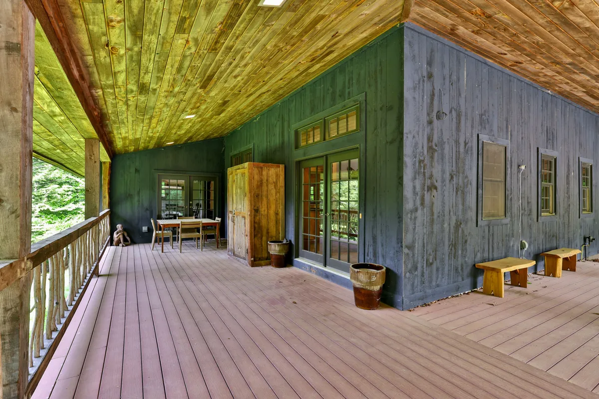 A spacious porch with wooden railing, dining table, large windows, potted plants, and views of wooded surroundings. The space is both functional and scenic, inviting guests to dine or relax while immersed in nature.