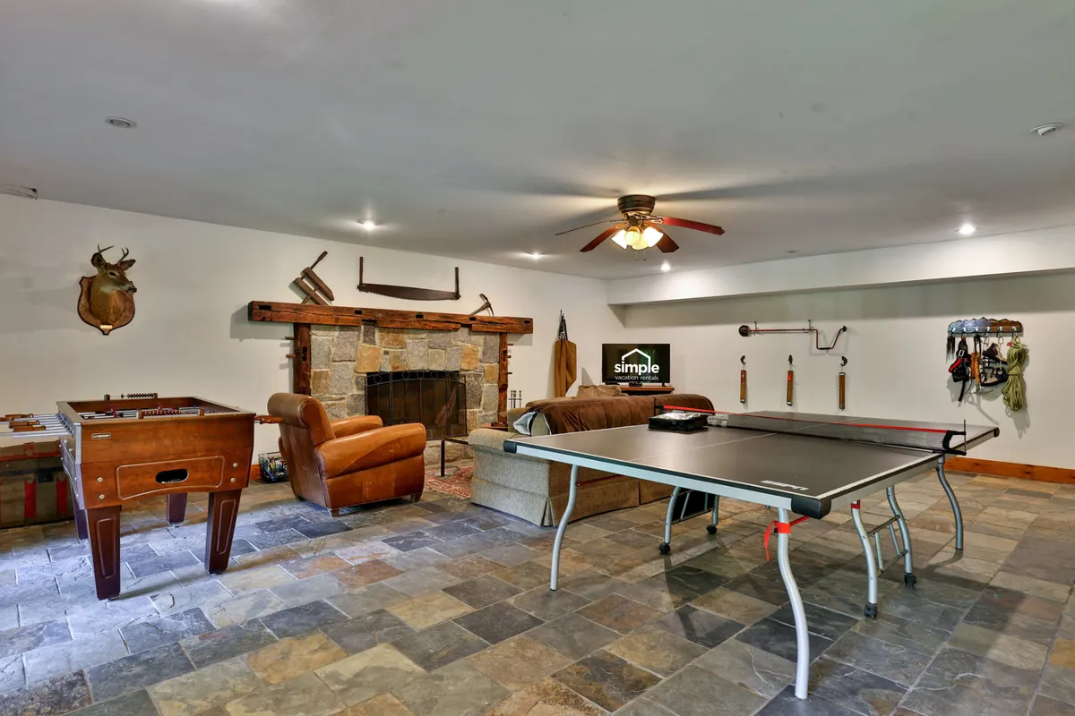 An inviting lower-level space with a stone fireplace, foosball table, ping pong table, and a plush couch. The room is arranged for group activities, games, and cozy relaxation by the fire.
