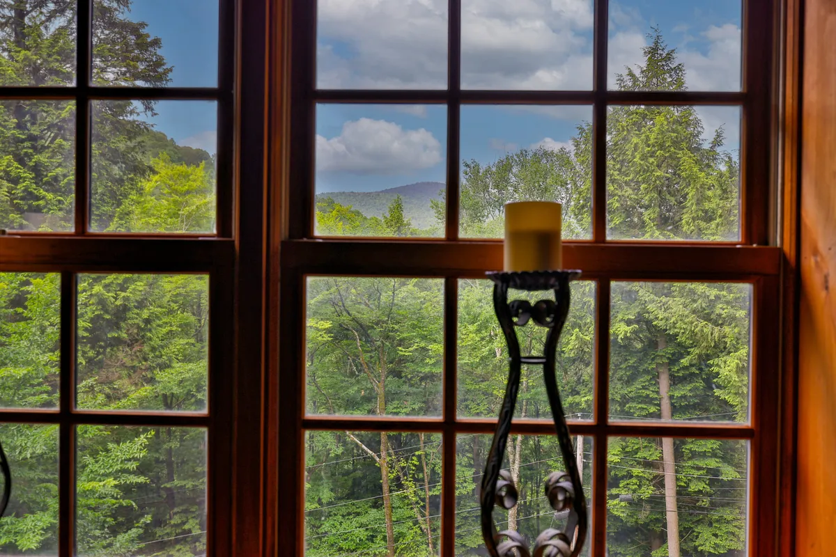 This image captures a large wooden window framing lush greenery outside, with a serene spot for morning coffee or reading a book. Early sunlight pours in, evoking a sense of connection to the mountain landscape beyond and inviting contemplation of the natural beauty surrounding the lodge.