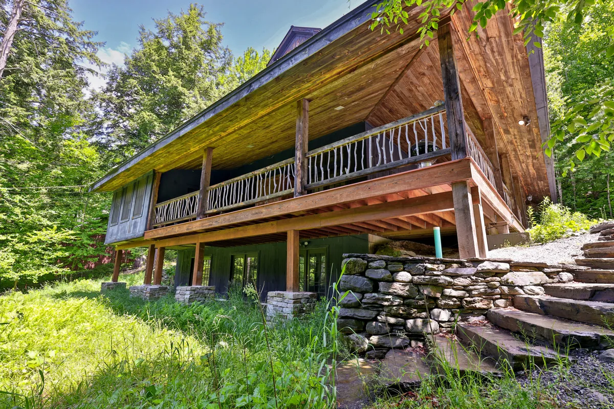 This image features the wooden porch of Bear Foot Lodge, stone steps leading down to lush greenery, and the surrounding natural landscape. The tranquil setting invites guests to relax outside, directly connecting the lodge with the outdoors and nearby trails.
