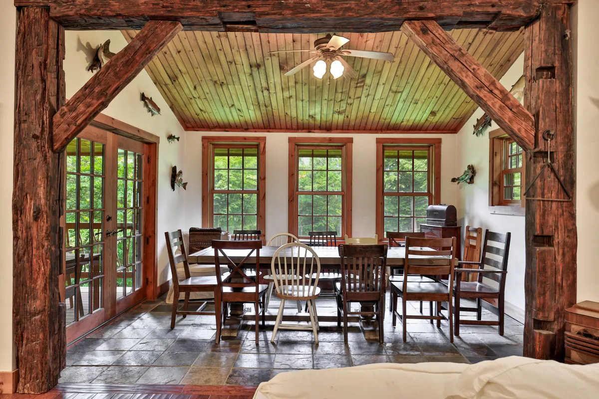 A large wooden dining table sits beneath exposed beams, surrounded by windows that fill the room with natural light. The setting is primed for group meals, festive gatherings, and memorable shared moments.