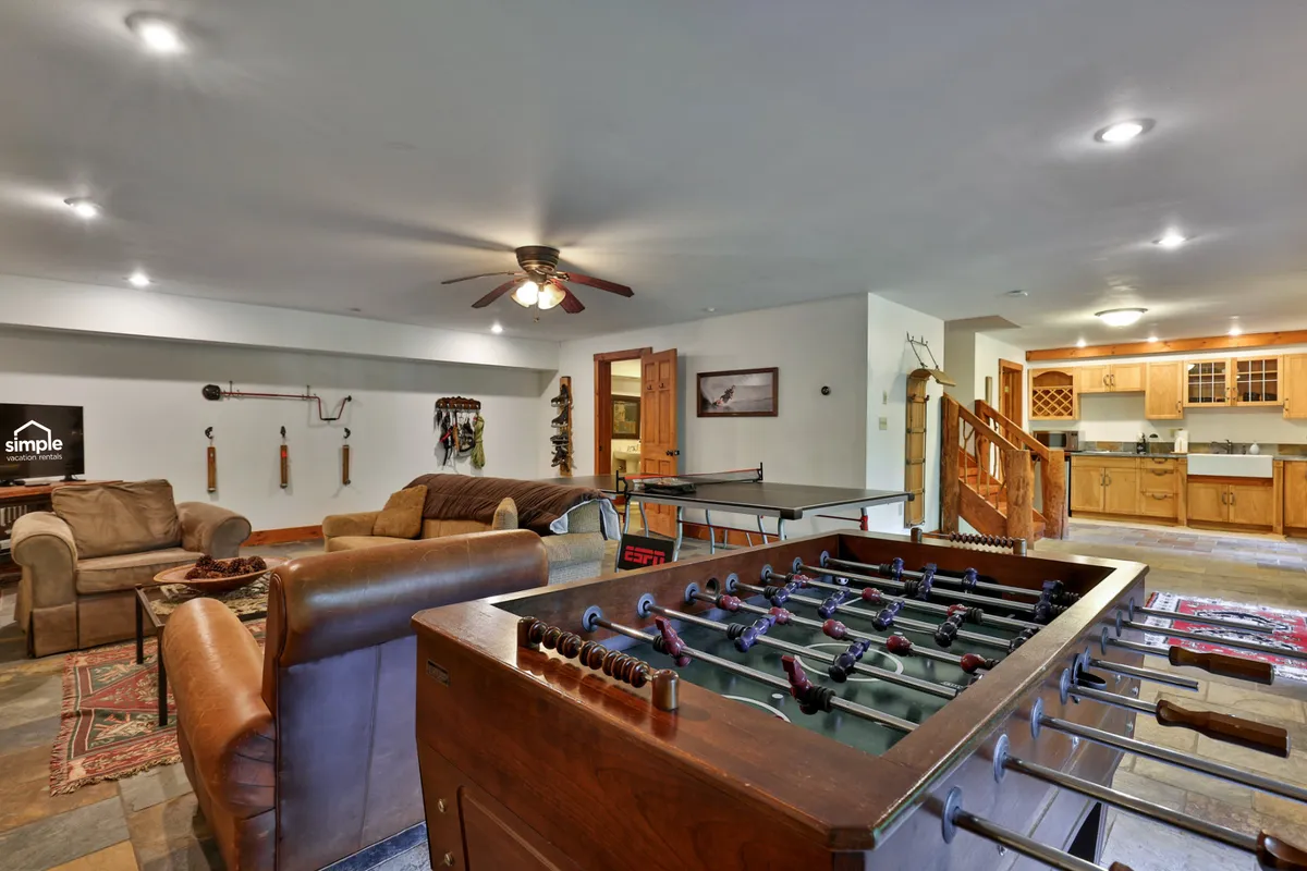 A lively recreation room featuring a foosball table, comfortable seating area, and a convenient kitchenette in the background. The space radiates a playful and cozy atmosphere, perfect for games, socializing, and casual snacks.